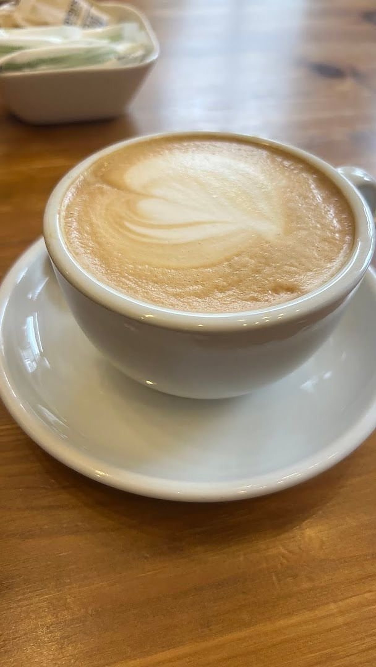 A white cup of milky coffee with latte art on a wooden table